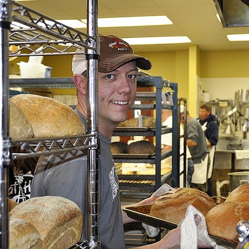 great harvest employee smiling and pulling loafs out of the oven